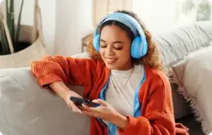 woman sitting on a couch on her phone with headphones.