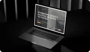 Laptop displaying an international search selection page on a dark desk in a dimly lit setting.