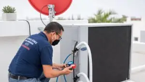 HVAC technician checks pressure gauges while servicing a rooftop air-conditioning unit in a bright, modern setting with clean white surfaces and red-and-blue accents.