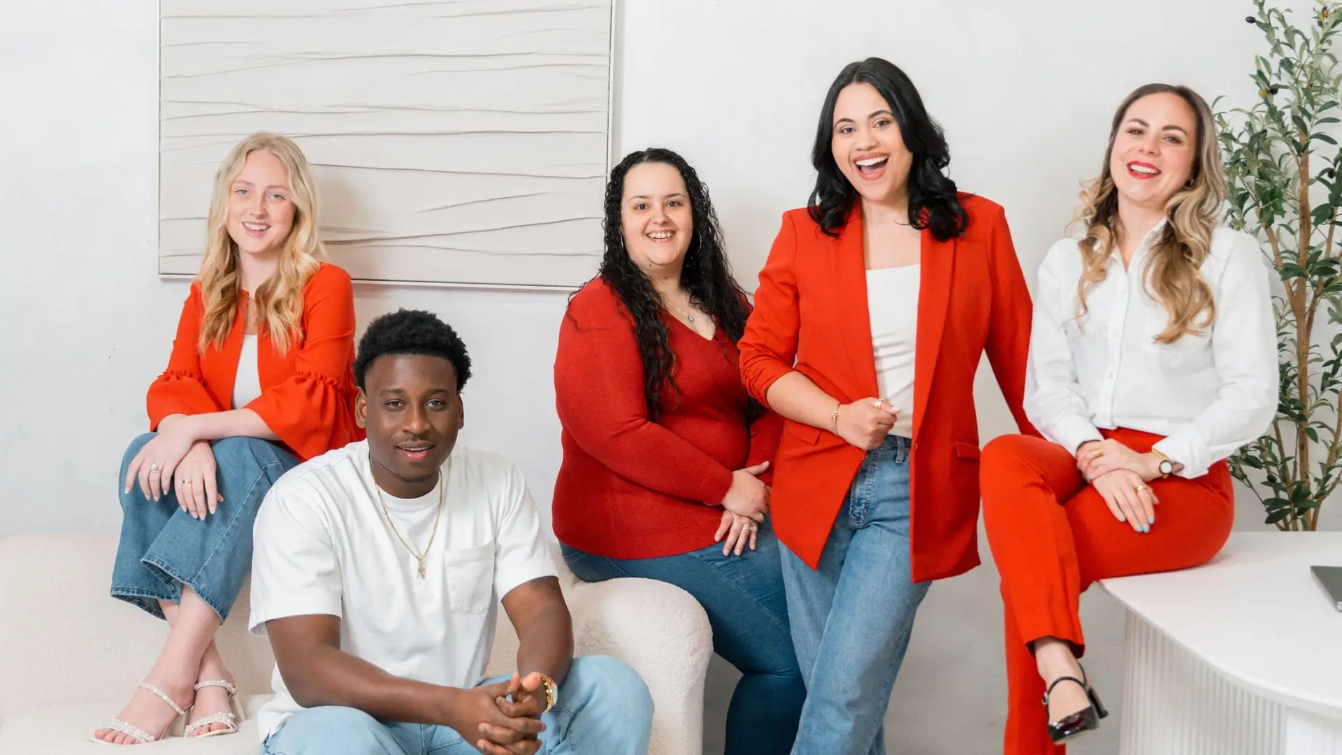 Five smiling marketing agency team members pose in a bright modern office, wearing coordinated red, white, and denim outfits.